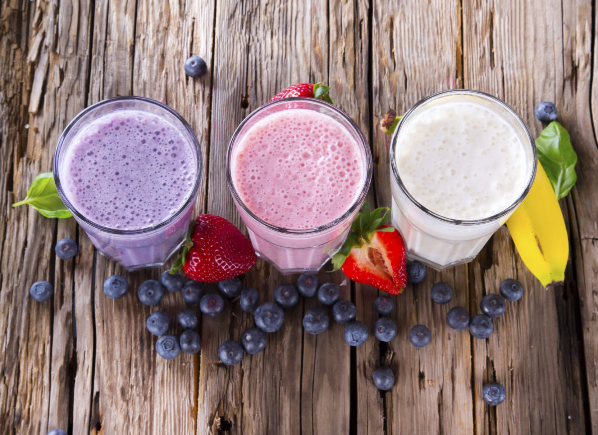 Fresh milk, strawberry, blueberry and banana drinks on wodeen table, assorted protein cocktails with fruits.