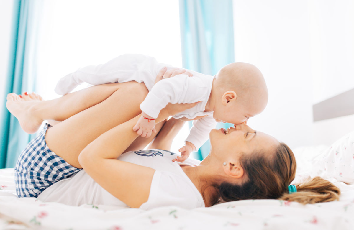 Happy woman playing with her baby boy and holding on knees